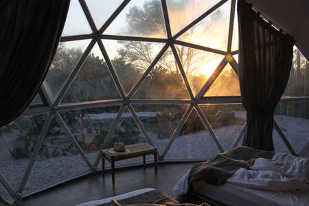 Couple lying in bed watching sunrise through glamping geodesic tent windowの写真素材