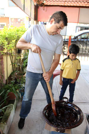 Latin dad and son cook together the traditional Mexican dish mole rojo in a clay pot with a wooden spoon as a family activity of pride, culture and traditionの写真素材