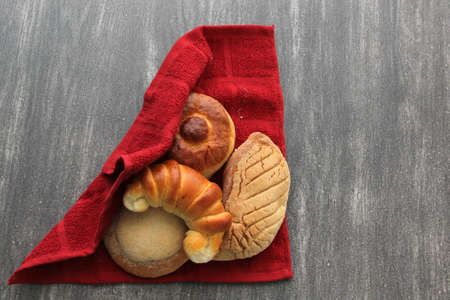 Mexican sweet bread such as biscuit, croissant, grating and fluffy worm, fresh, freshly made at home on a wooden table with napkin and basketの写真素材