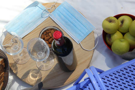 stylish picnic in pandemic. vintage basket with wine, food fruit seeds and protective masks clinical...