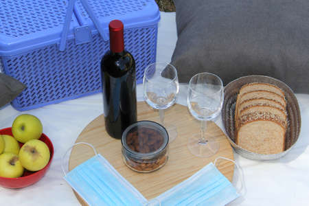 stylish picnic in pandemic. vintage basket with wine, food fruit seeds and protective masks clinical...