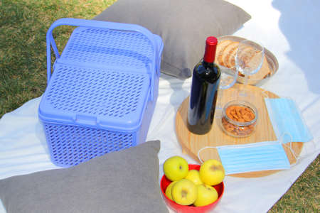 stylish picnic in pandemic. vintage basket with wine, food fruit seeds and protective masks clinical useの写真素材