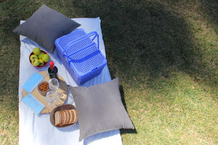 stylish picnic in pandemic. vintage basket with wine, food fruit seeds and protective masks clinical useの写真素材