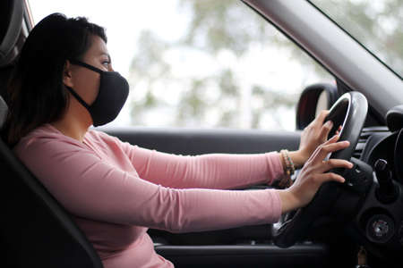 latin woman driver with protection mask in vehicle interior, new normal when drivingの写真素材