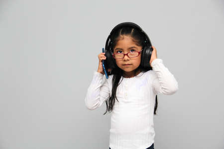 4-year-old brunette Latin girl with glasses listens to music in her headphones connected to her cell phone dances, sings and enjoys the rhythm happy and excitedの写真素材
