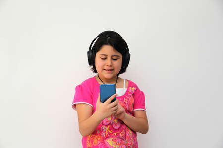 10-year-old Hispanic girl listens to music on her headphones connected to her cell phone dances, sings and enjoys the rhythm happy and excitedの写真素材