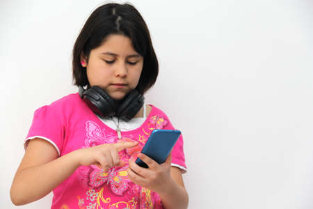 10-year-old Hispanic girl listens to music on her headphones connected to her cell phone dances,...
