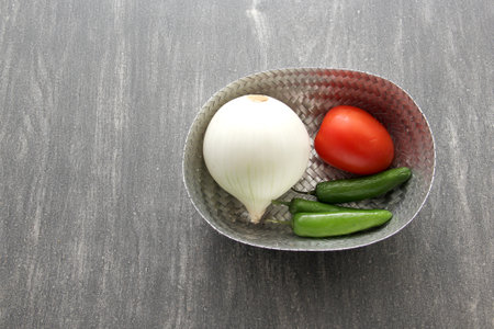 Variety of fresh vegetables in basket and chopping board ready to cook a Mexican sauce: onion, tomato, green chiliesの写真素材