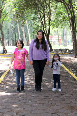 Single and divorced Latin mom and daughters walk in the park outdoors alone spend quality family time on summer vacation or weekendの写真素材