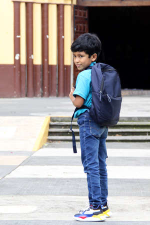 Poor dark-haired 8-year-old Latin boy walks down the street on his way to study back to school with...
