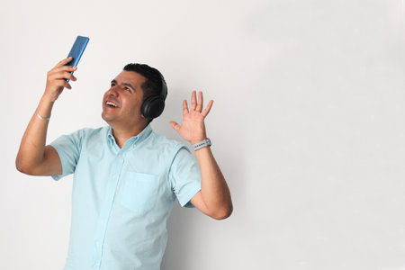 Latino adult man uses technology with his cell phone and headphones to listen to music, play video games, make video calls, watch series, and date on the appの写真素材