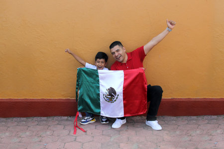 Latin Mexican dad and son show the flag of Mexico very proud of their culture and tradition, to celebrate the national holidays of Independence in September, Revolutionの写真素材
