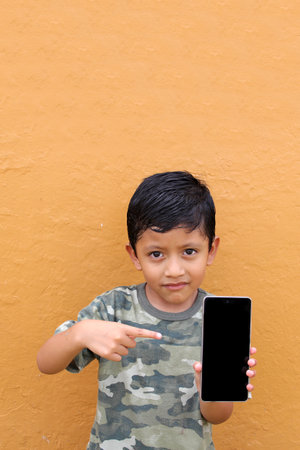 Latin child boy over isolated yellow background with cell phone in victory position shows happy and excitedの写真素材
