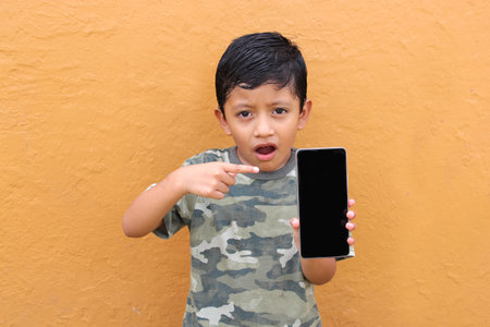 Latin child boy over isolated yellow background with cell phone in victory position shows happy and excitedの写真素材
