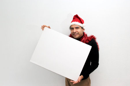 Latino adult man with hat and Christmas garland shows banner and blank notebook to put a message of congratulations, love or wish listの写真素材