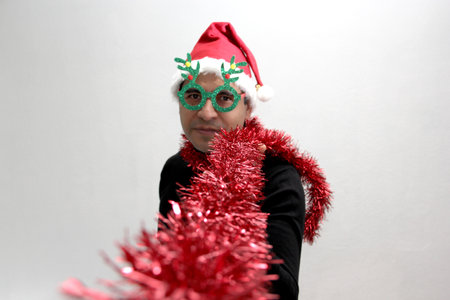 Dark-haired Latin adult man with Christmas hat, wreath and glasses shows his enthusiasm for the arrival of December and celebrating Christmas and New Yearsの写真素材