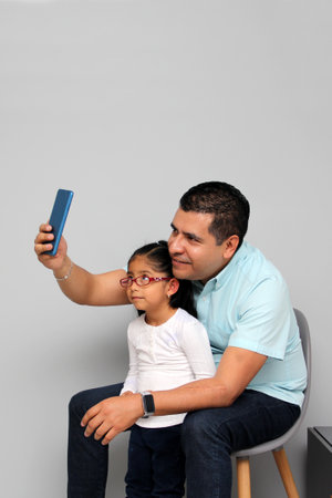 Single divorced Latino dad and daughter use cell phone to video call, take selfies, play video games, and shop onlineの写真素材