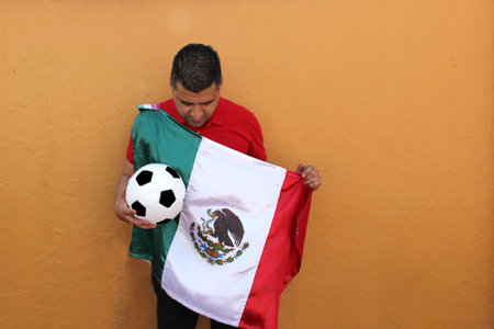 Mexican adult man plays with a soccer ball very excited that he is going to see the game with de mexican flag and wants to see his team winの写真素材