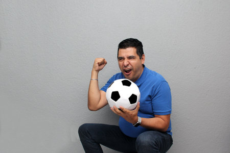Latino adult man plays with a soccer ball very excited that he is going to see a game and wants to see his team winの写真素材