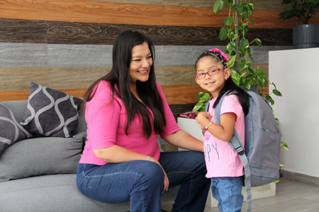 Latin mom with her 4 year old daughter who wears glasses prepare to go back to school with backpack vacations endの写真素材