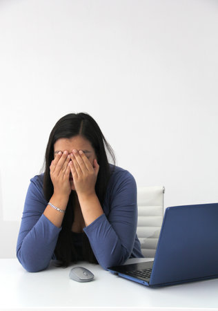 Dark-haired latin adult woman works in her office with laptop with a lot of stress having a headache with a migraine and suffering from tiredness, depression, anxiety and burnoutの写真素材