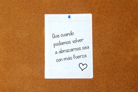 White note on cork board with message in Spanish "That when we can hug each other again it will be with more strength"の写真素材
