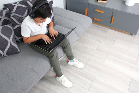 9-year-old Hispanic boy plays video games on his laptop with headphones leading to being overweight...