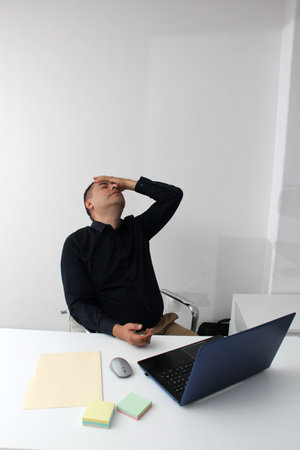 Latino adult man works in his office with his laptop, his head, neck, and back, cervical, lumbar...