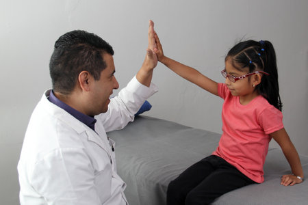 Pediatrician doctor and 4 year old latin girl patient in consultation are friends and make hi five sign and bump fistsの写真素材