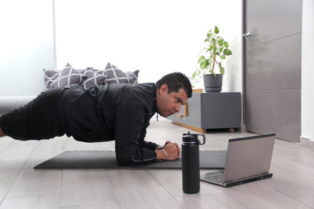 Overweight latino adult man exercises inside his home in his living room via computer online to be healthyの写真素材
