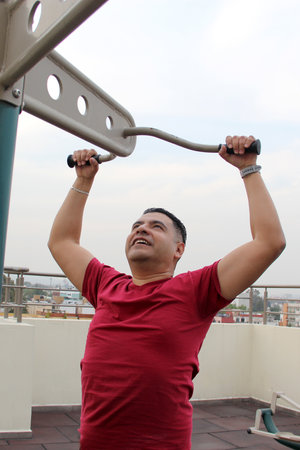 Adult 40-year-old Latino man exercises on the roof garden of her apartment with shared public...