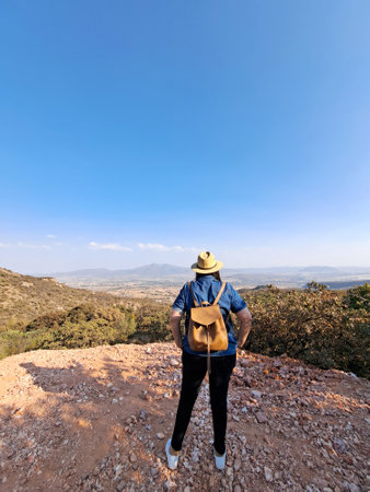 Adult woman with hat looks towards the horizon on top of a mountain opens his arms and breathes in front of the mountainous landscape proud of her achievementの写真素材