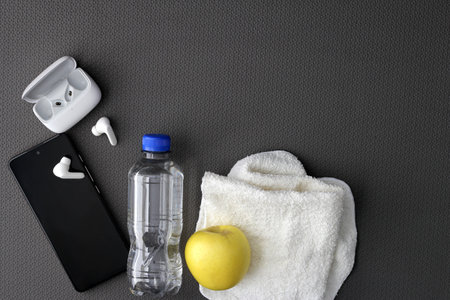 Mat to exercise with the necessary objects such as wireless headphones, cell phone, apple, water to hydrate, sweat towel and locker keysの写真素材