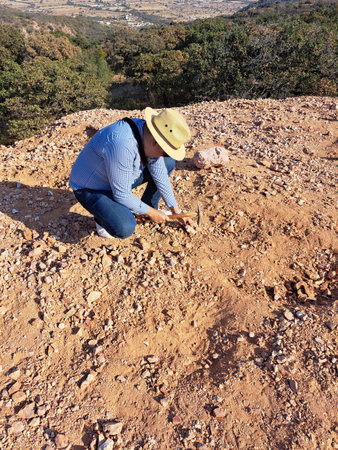 Latin man with hat and miner's pick hammer works as a geologist, studies the composition and structure of the mineral soil of the mountainの写真素材
