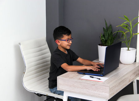 7-year-old Latino boy with glasses does home schooling takes online classes at home on a desk with a...