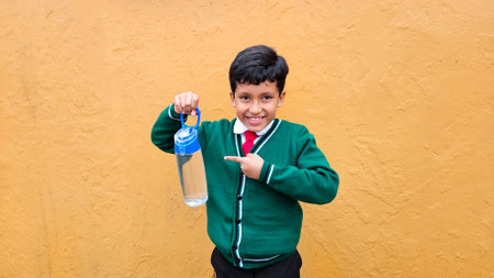 Dark-haired 9-year-old Latino boy in elementary school uniform drinks water because it is important to hydrate on hot daysの写真素材