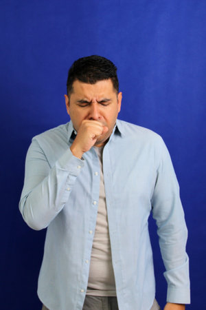 Dark-haired Latino adult man is sick, has a sore throat and suffers from strep cough and tonsil infectionsの写真素材