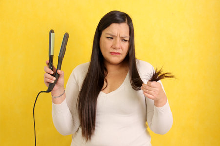 Adult Latina woman with very long straight hair combs her hair with a straightener worried about the damage it causes to split endsの写真素材
