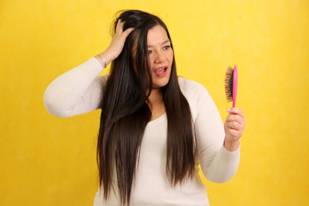 Adult Latina woman with very long hair worries and suffers while brushing because her hair falls out, is dry, damaged, has split ends and knots to untangleの写真素材