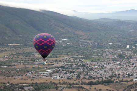 Colorful hot air balloons at sunrise soaring over vegetation and urban landscapeの写真素材