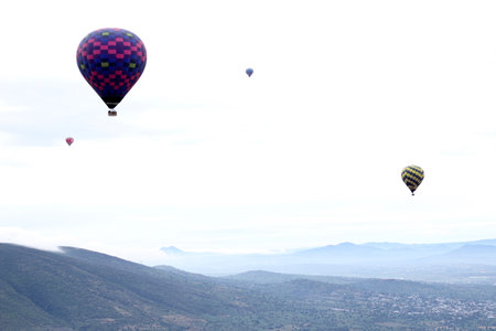 Colorful hot air balloons at sunrise soaring over vegetation and urban landscapeの写真素材