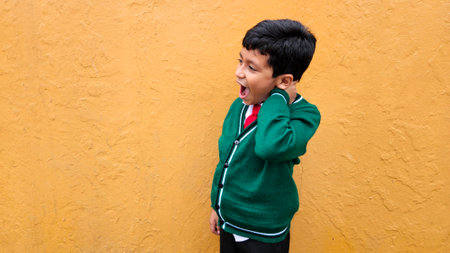 9-year-old dark-skinned Latino boy in school uniform suffers from back and neck pain from carrying a heavy backpack has muscle strainの写真素材