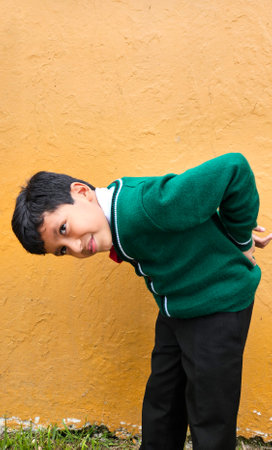 9-year-old dark-skinned Latino boy in school uniform suffers from back and neck pain from carrying a heavy backpack has muscle strainの写真素材