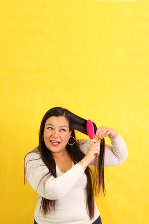 Adult 40-year-old Latina woman brushes her hair with difficulty because it is very tangled due to knots caused by drynessの写真素材