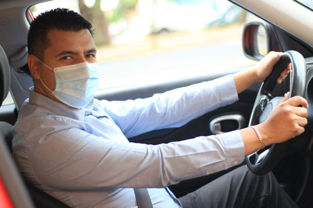Latino man driver with covid-19 protection mask driving inside carの写真素材