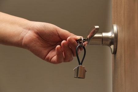 Keys with keyring in the shape of a house open door as a concept of real estate delivery of a new...