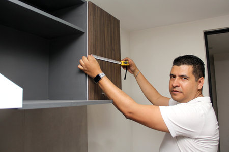 Dark-haired 40-year-old Latino man takes measurements of newly installed kitchen cabinets as a workerの写真素材