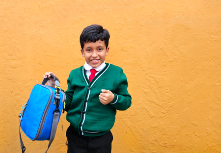 Dark-haired 9-year-old Latino boy in a school uniform shows off his new lunch box that he will bring back to schoolの写真素材