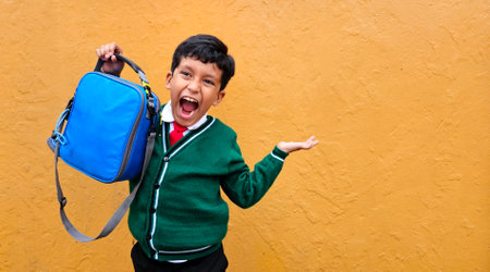 Dark-haired 9-year-old Latino boy in a school uniform shows off his new lunch box that he will bring back to schoolの写真素材