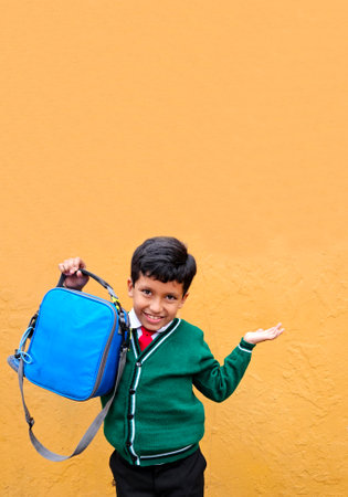 Dark-haired 9-year-old Latino boy in a school uniform shows off his new lunch box that he will bring...